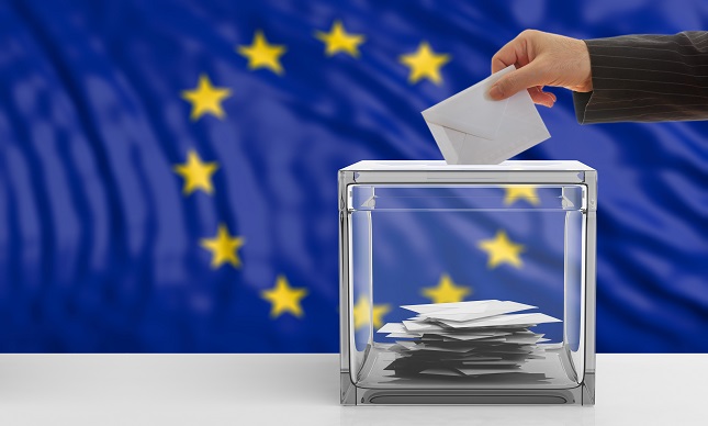 Wahlurne mit eingeworfem Wahlbrief im Hintergrund Europaflagge